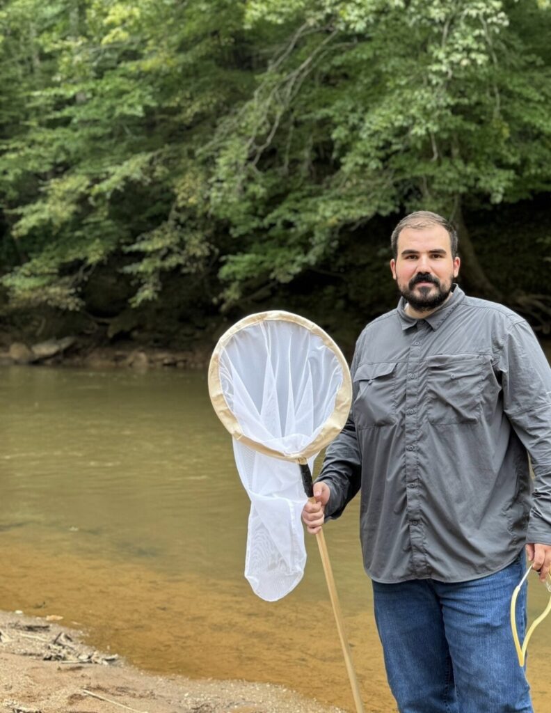 A photo of Mohamad Hamdan standing in front of a creek and holding a net.